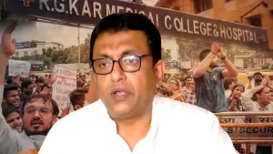 A man in a white shirt and glasses with a protest at R.G. Kar Medical College and Hospital in the background